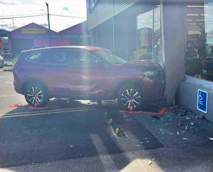 Large red SUV smashed into the wall of supermarket with shards of glass scattered all around car park.