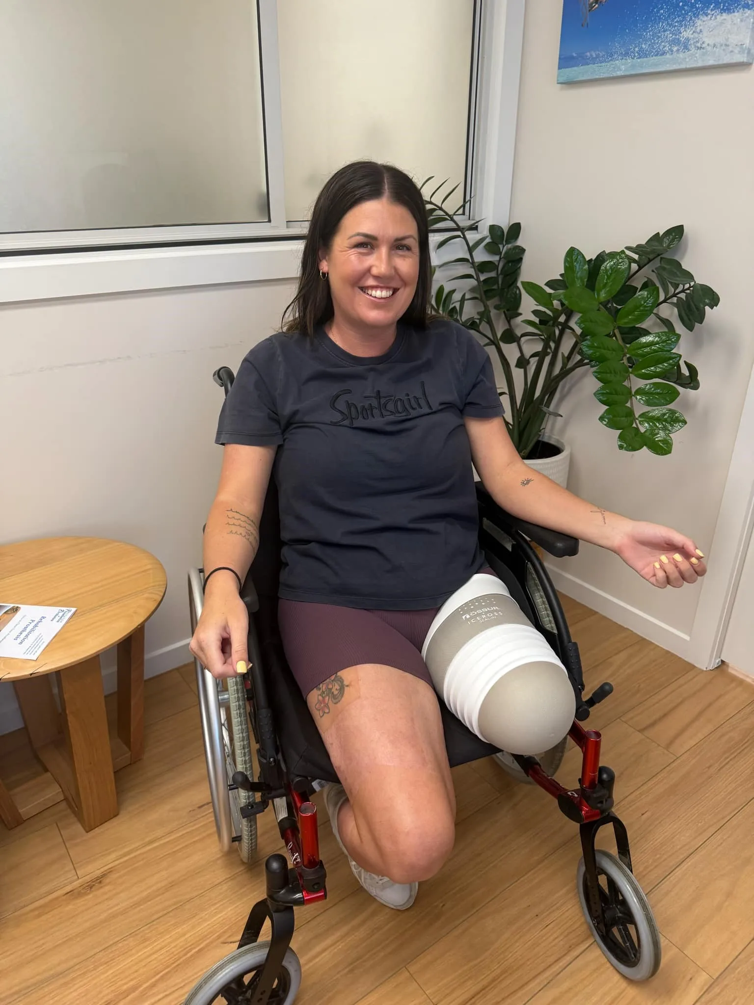 Woman wearing black top and red shorts sitting on wheelchair with left leg amputated above the knee, smiling at camera.