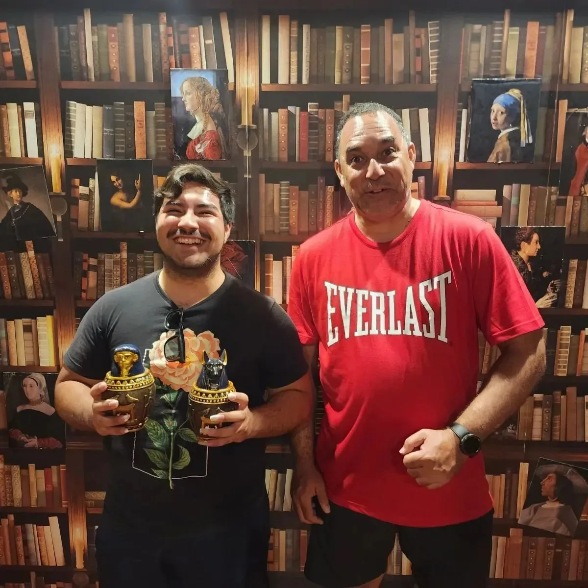 man in red shirt and man in black shirt in room full of books
