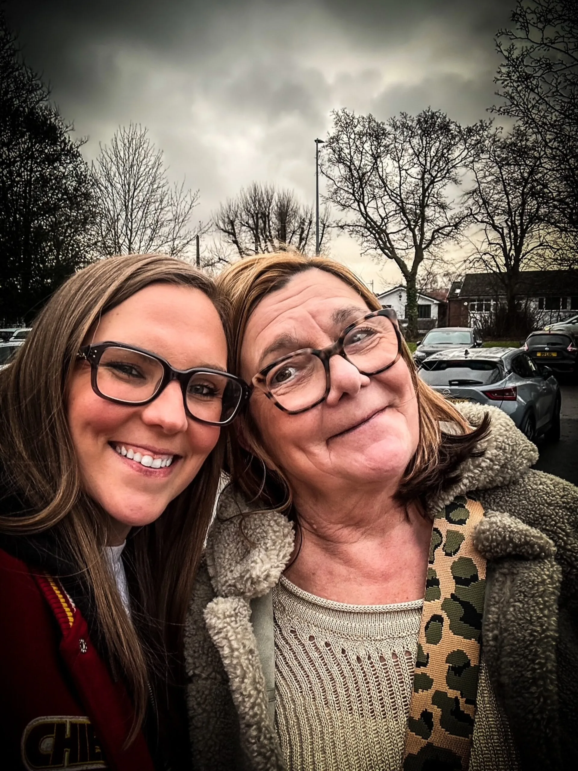 Left: Woman with long hair wearing glasses smiling at camera while standing next to another woman.
Right: Woman with short blonde hair and glasses smiling at camera. 