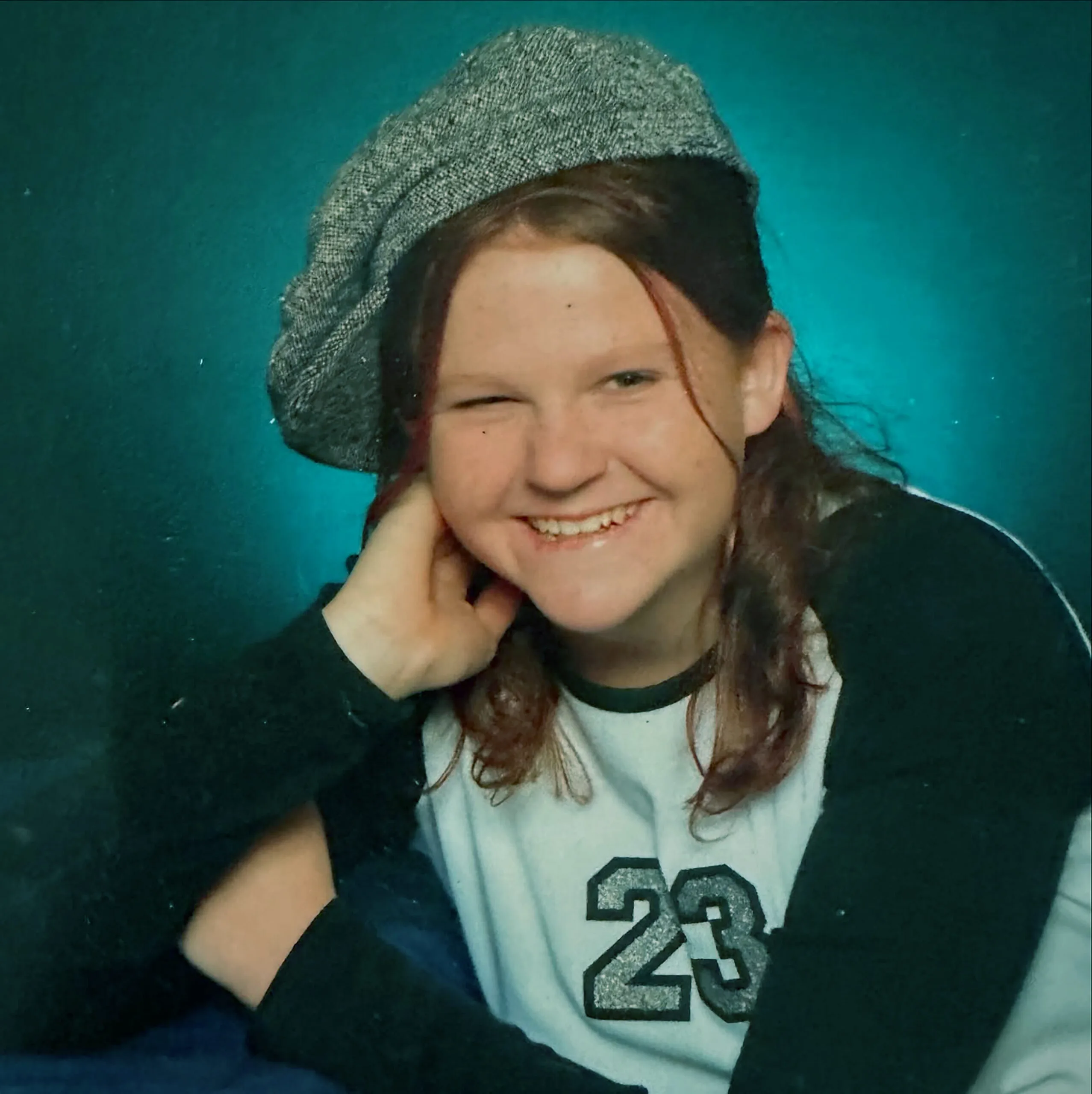Young girl with red hair, wearing grey beret, winking at camera.