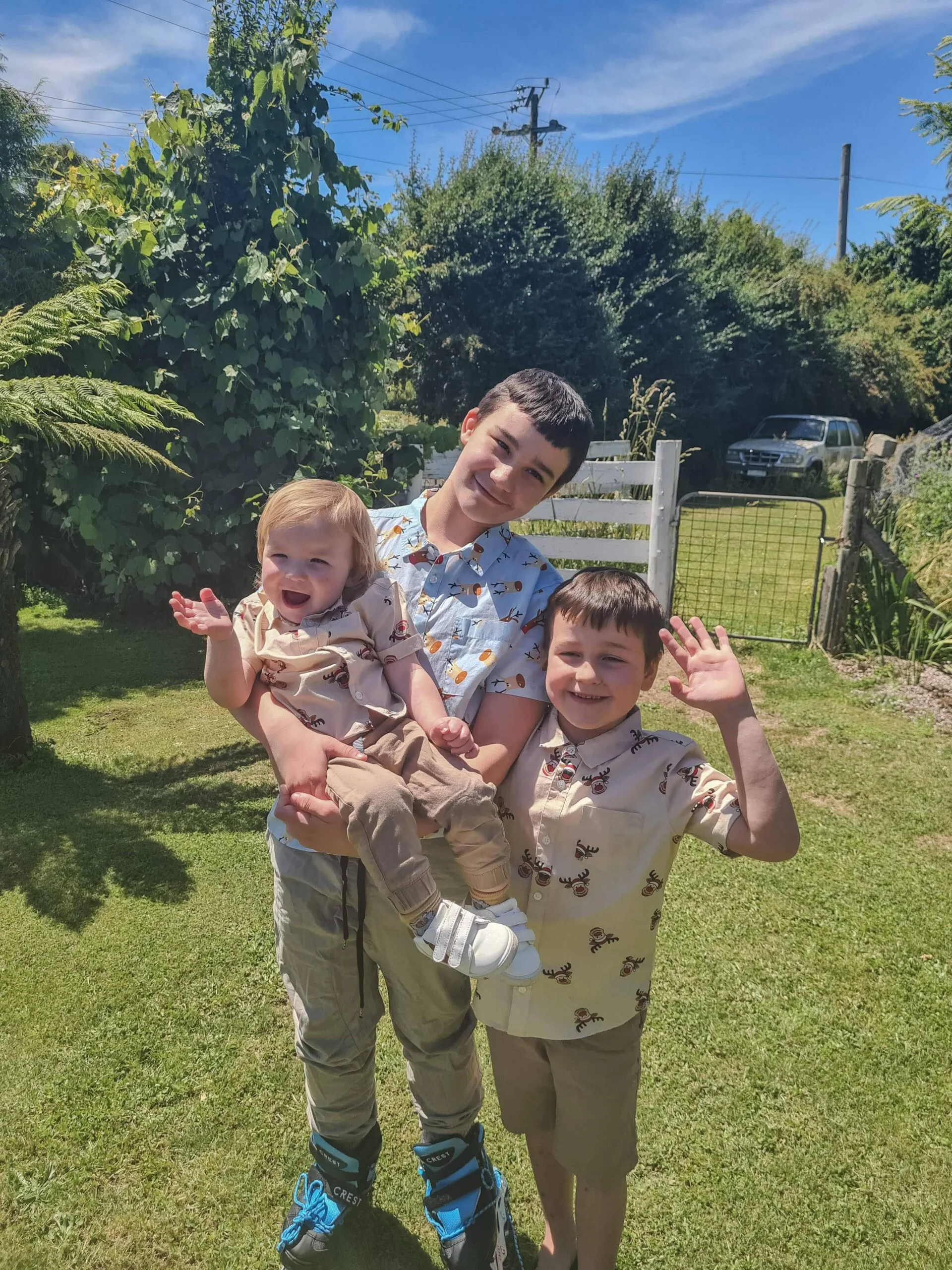 A taller boy wearing blue holds his younger brother, his other brother on the right is smiling