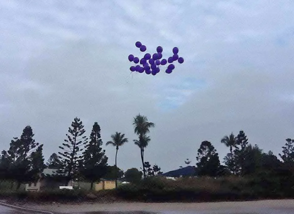 Purple balloons flying into the sky over he beach.