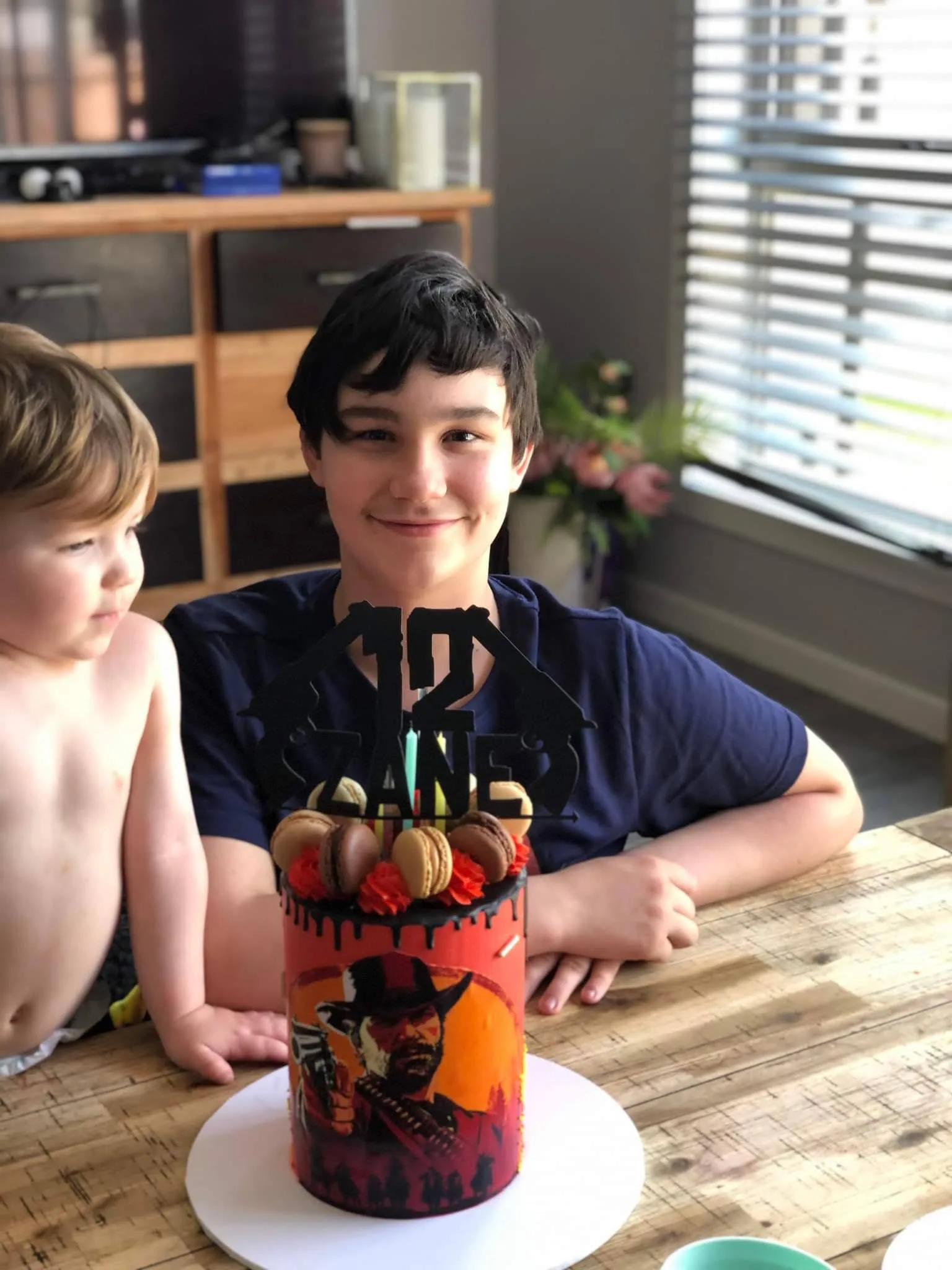 a boy with brown hair and a navy shirt sits in front of a 12th birthday cake