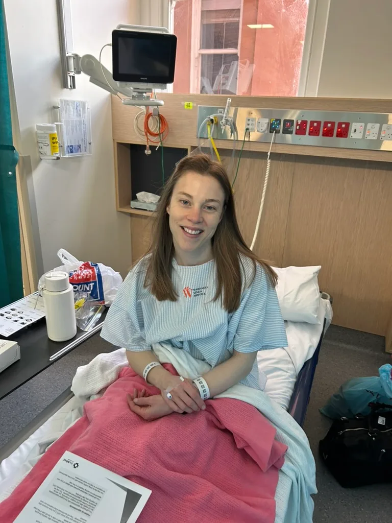 a girl in hospital bed wearing hospital gown with pink blanket