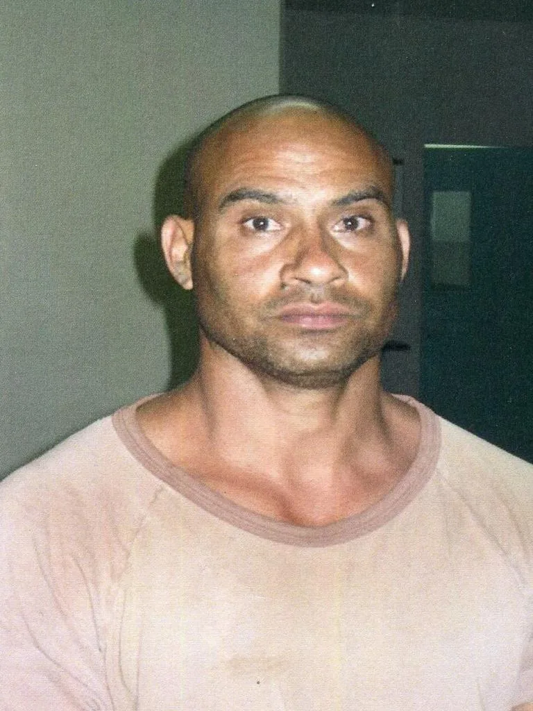 Man wearing beige shirt, staring into camera with unamused facial expression.