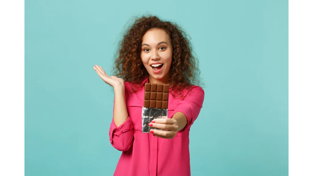 An excited woman holds out a chocolate bar.