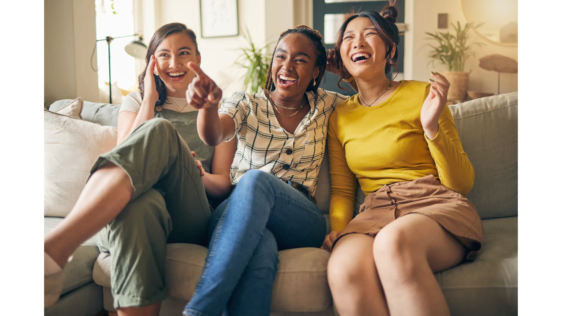 Three female friends sit on a couch and share a laugh.