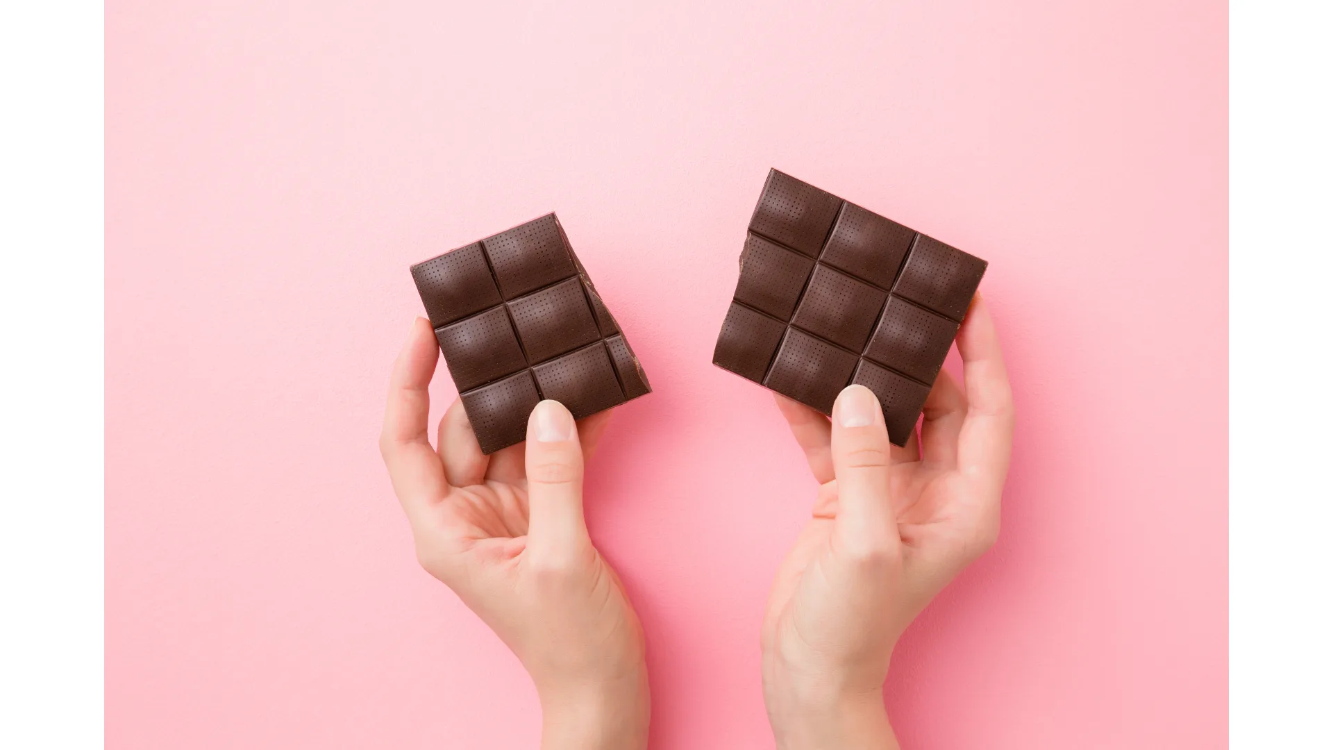 A pair of hands breaks apart a block of dark chocolate.