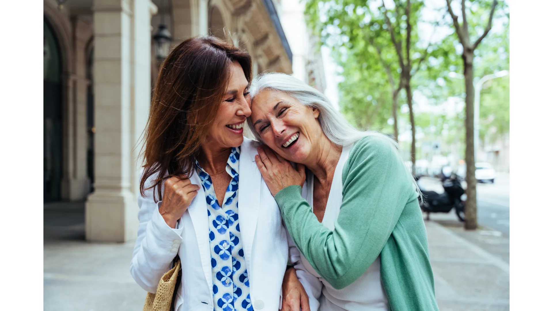 Two older women share a laugh while strolling down a street.