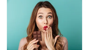 A surprised woman holds a block of dark chocolate.