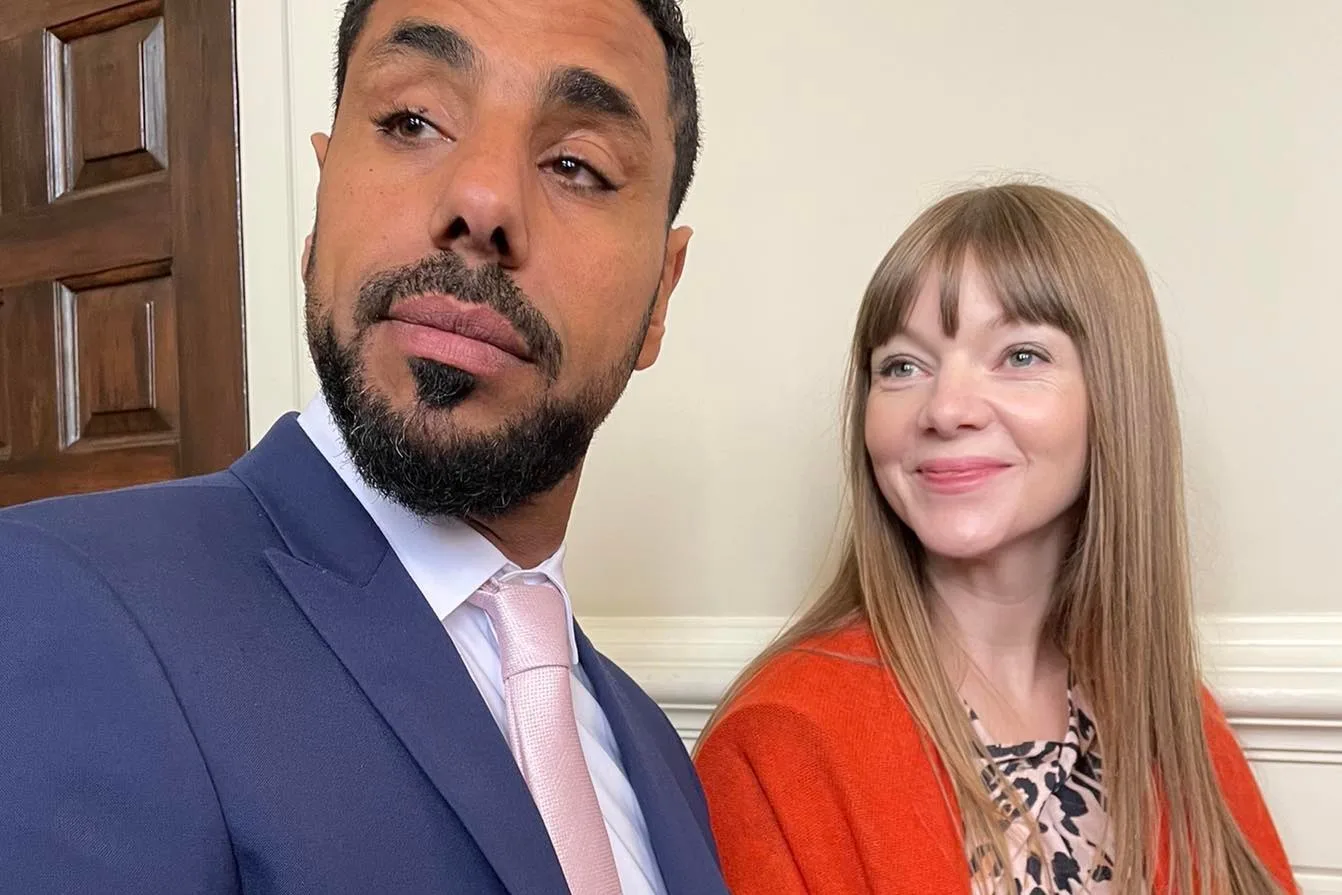 woman in organe top and man in blue suit both looking left 