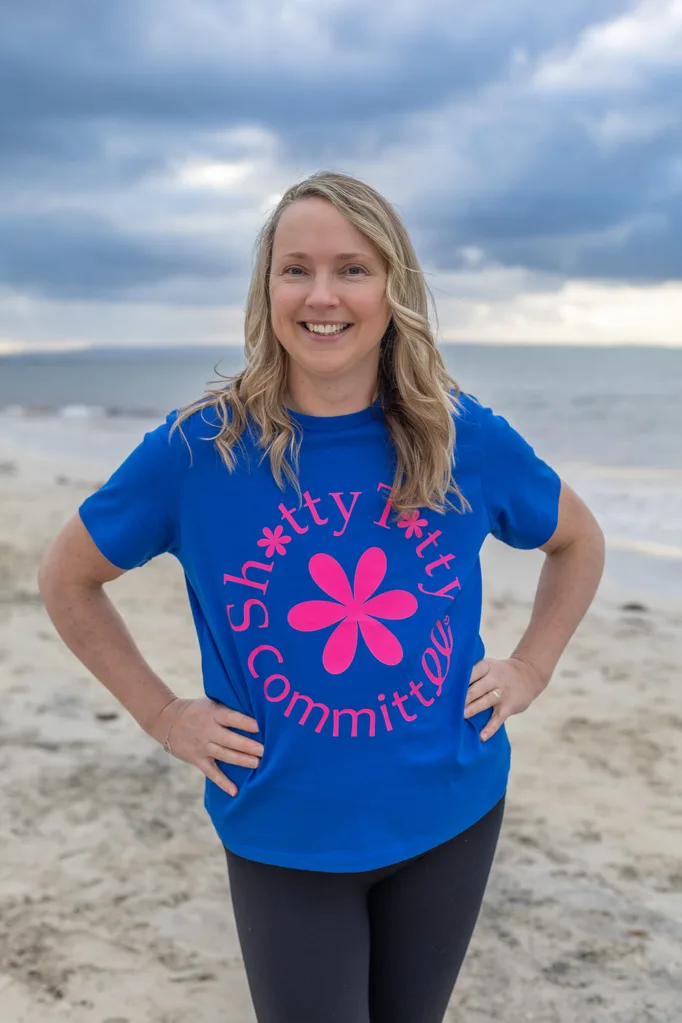 woman in blue tshirt with pink flower design standing on a beach.