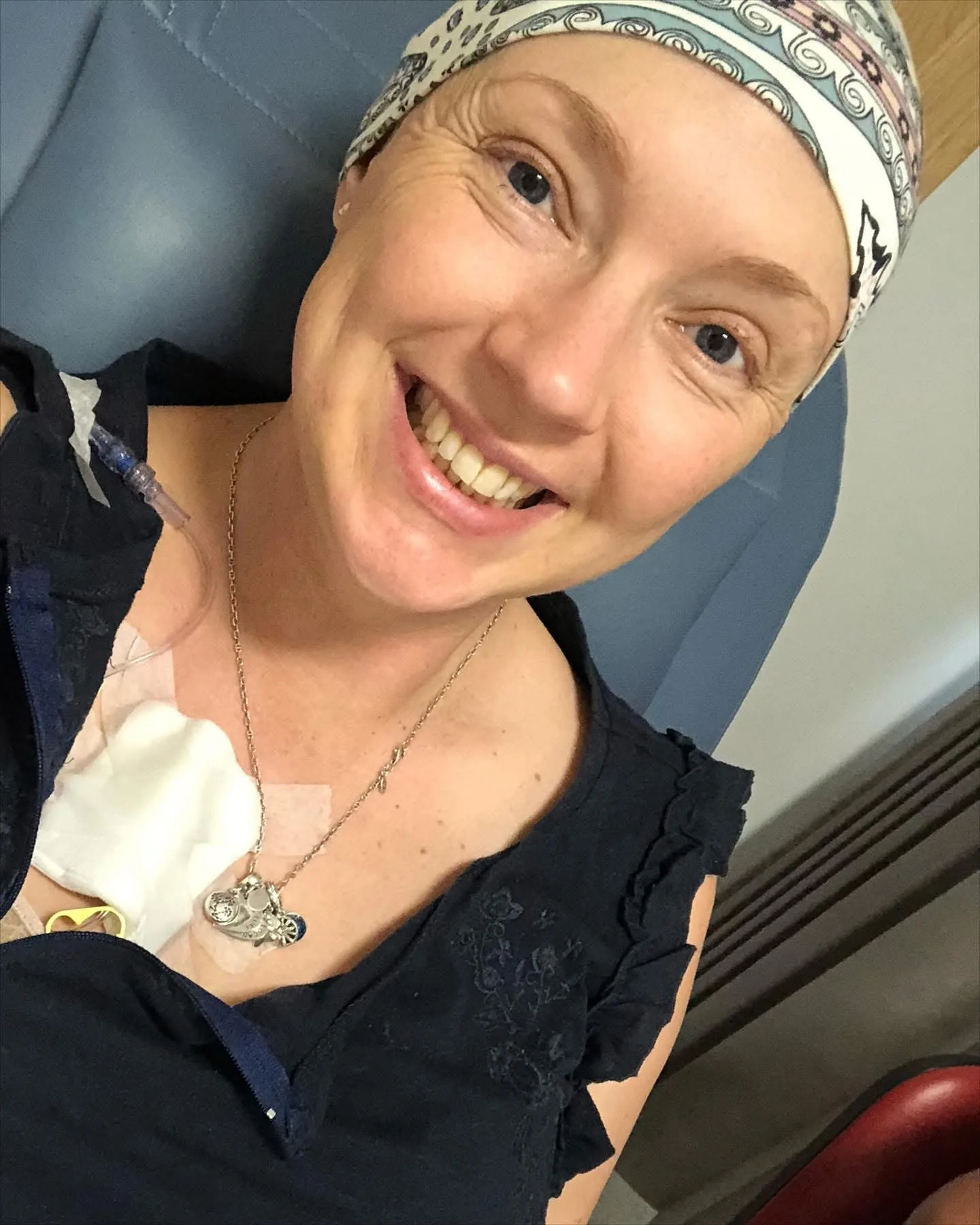 woman in black top smiling in head scarf with bandage on chest 