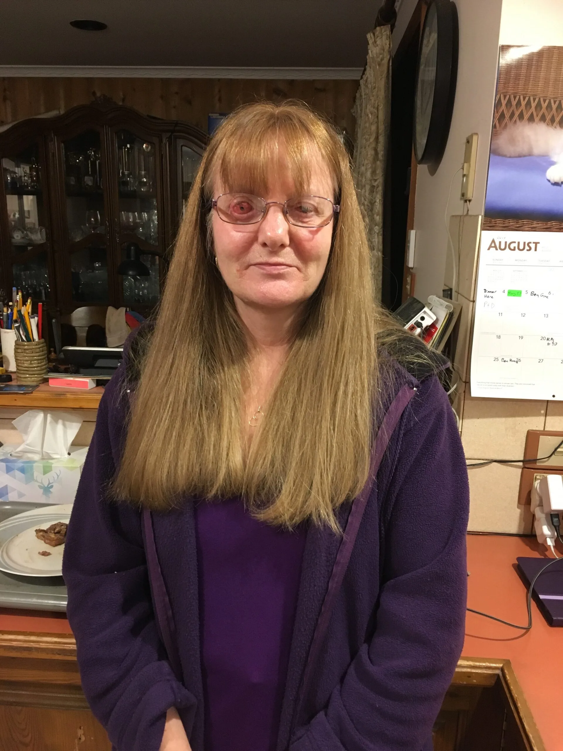 A woman with a large eye and glasses she is inside and has long hair and a fringe