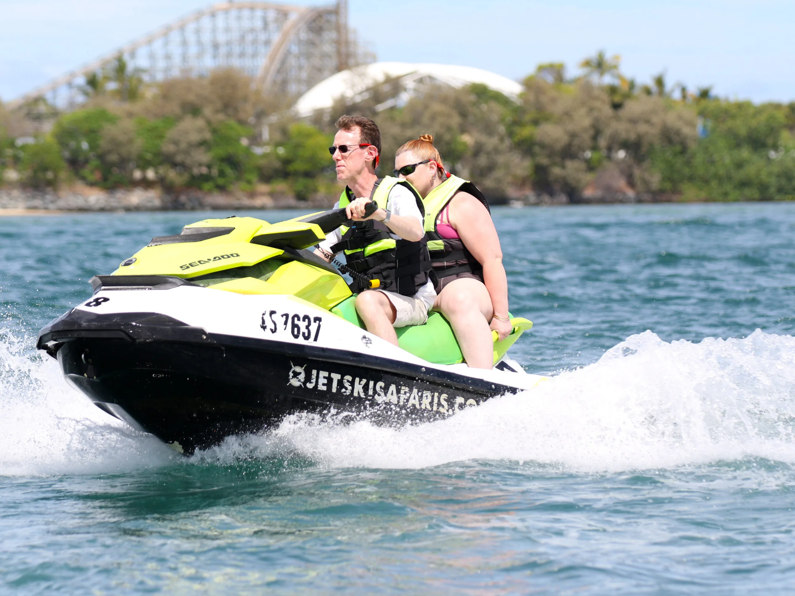 Man and woman wearing vests and sunglasses on green jetski in the ocean.
