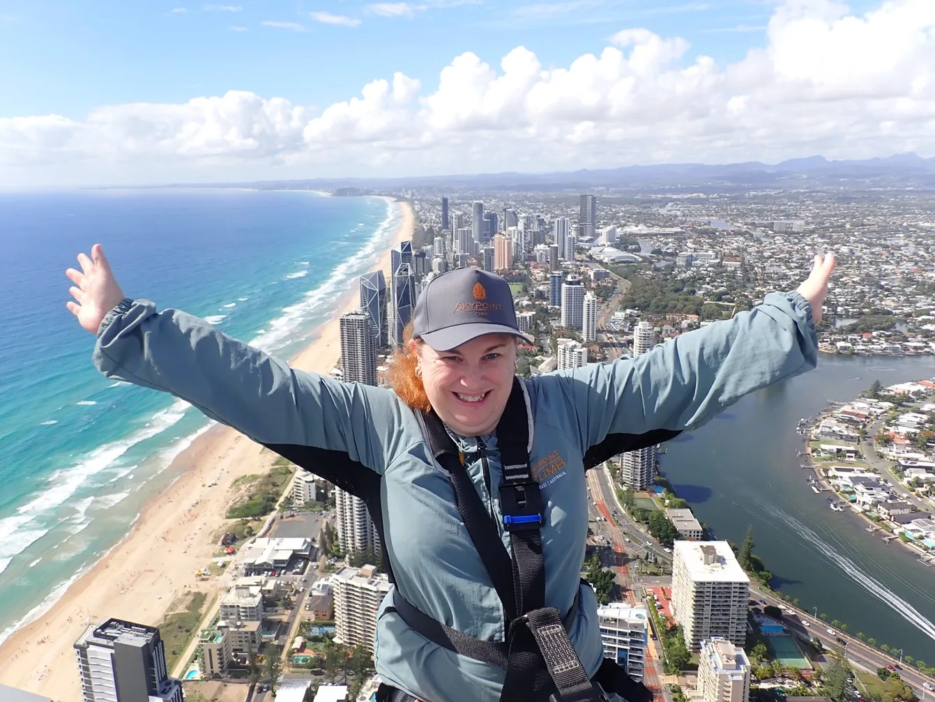 Woman wearing blue jacket and blue hat, with city landscape in the background smiling at camera.