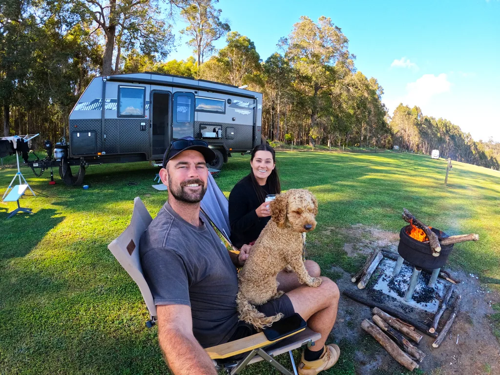 Man. dog and woman sitting round an outdoor fire