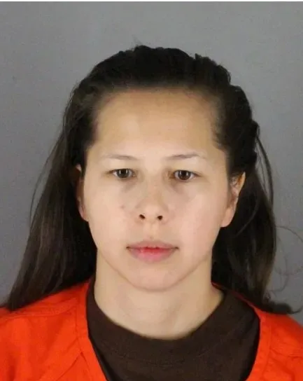 Woman with black hair slicked back, wearing prison clothes, staring down at camera.