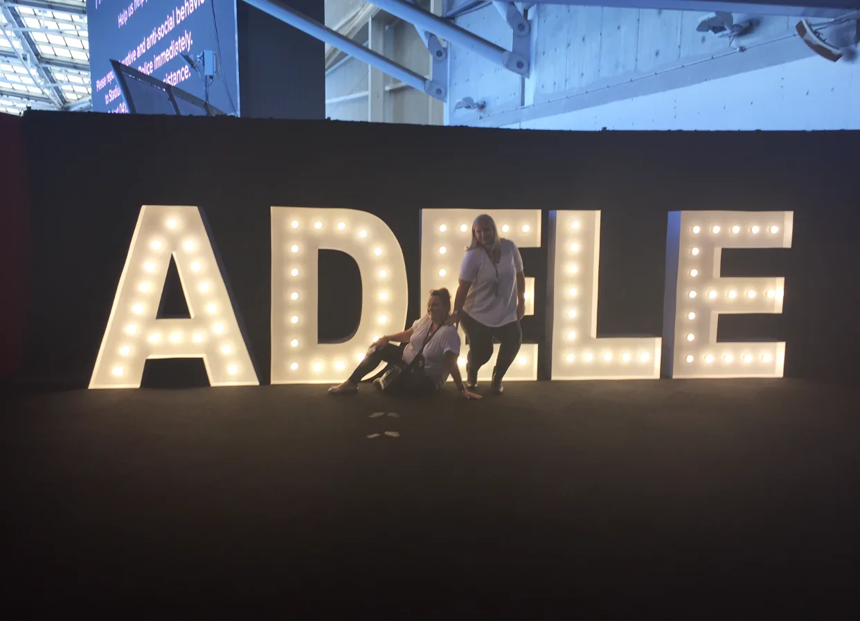 name ADELE in lights with two women in front 