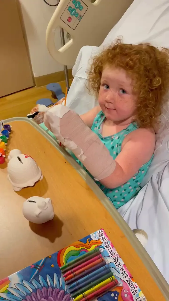 Girl with red curly hair laying in hospital bed with arm completely bandaged up.