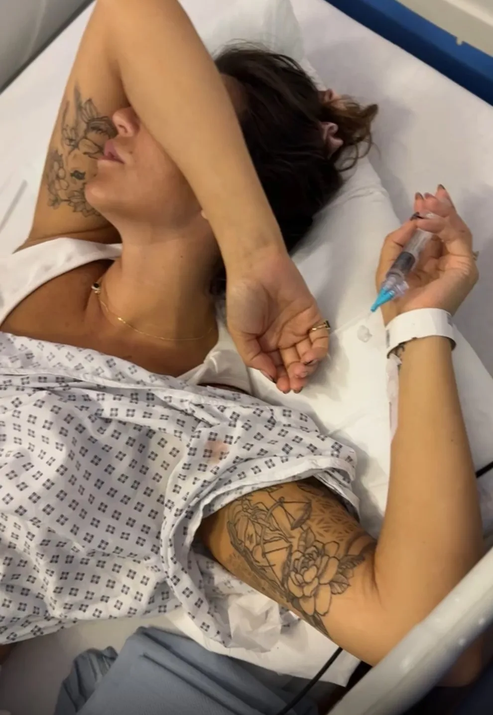 Woman with brown hair covering face with arm laying in hospital bed.