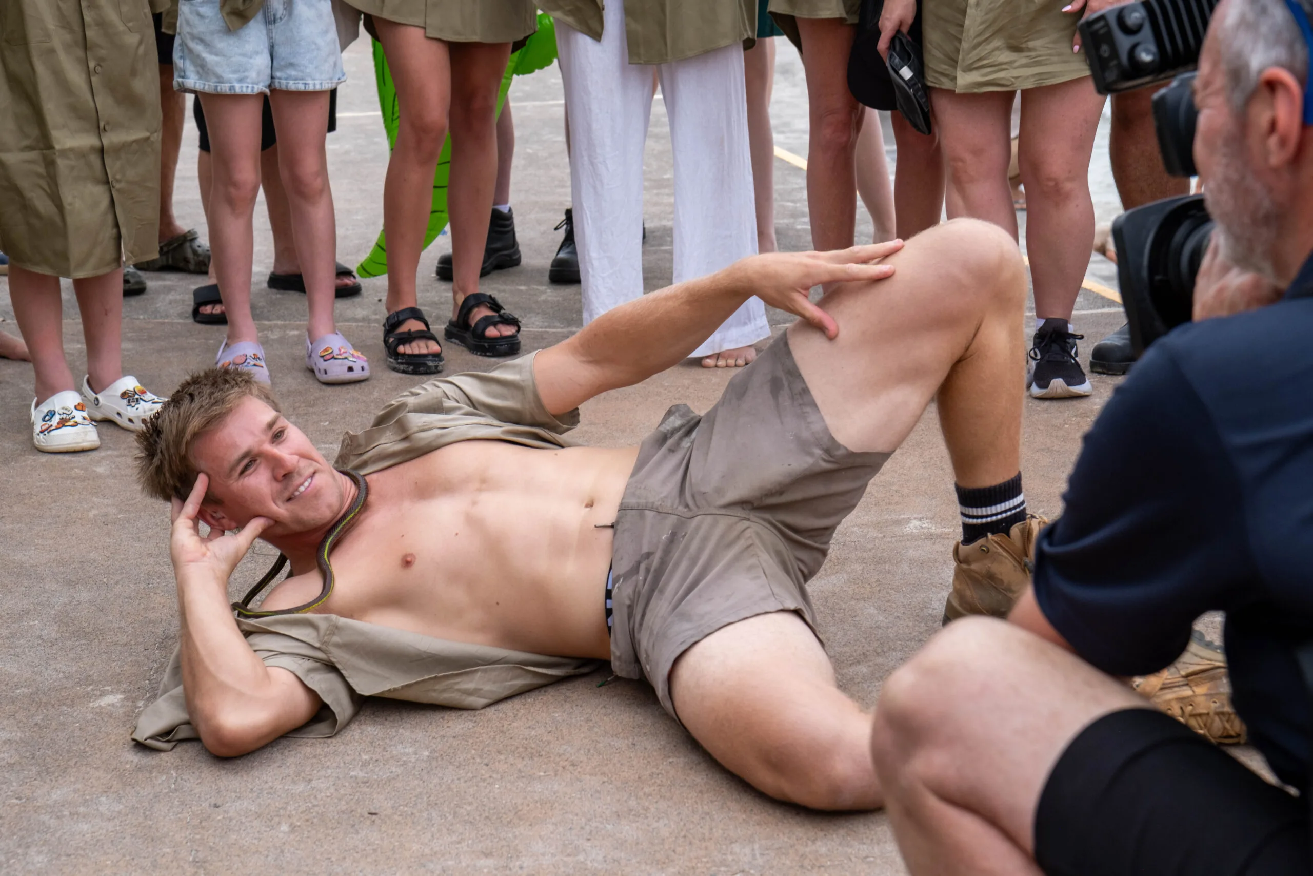 Man in khaki shirt and shorts laying on floor posing