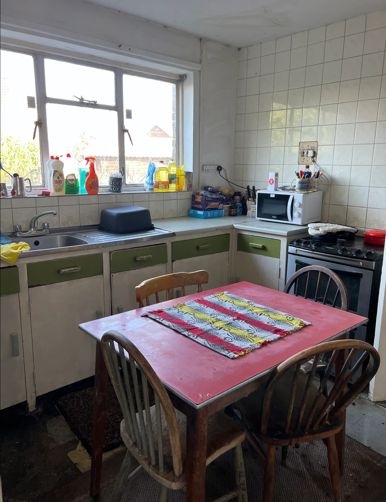 Photo of clean kitchen, pink table with brown chairs and clean gas stove top.
