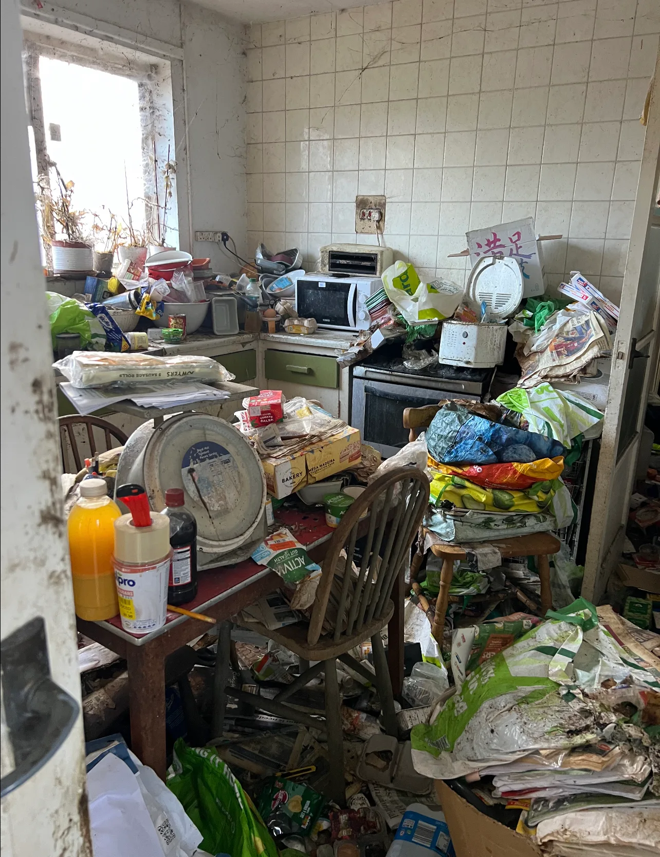 Picture of kitchen with rubbish strewn across the floor, table piled up with junk and furniture covered in mould and dust.