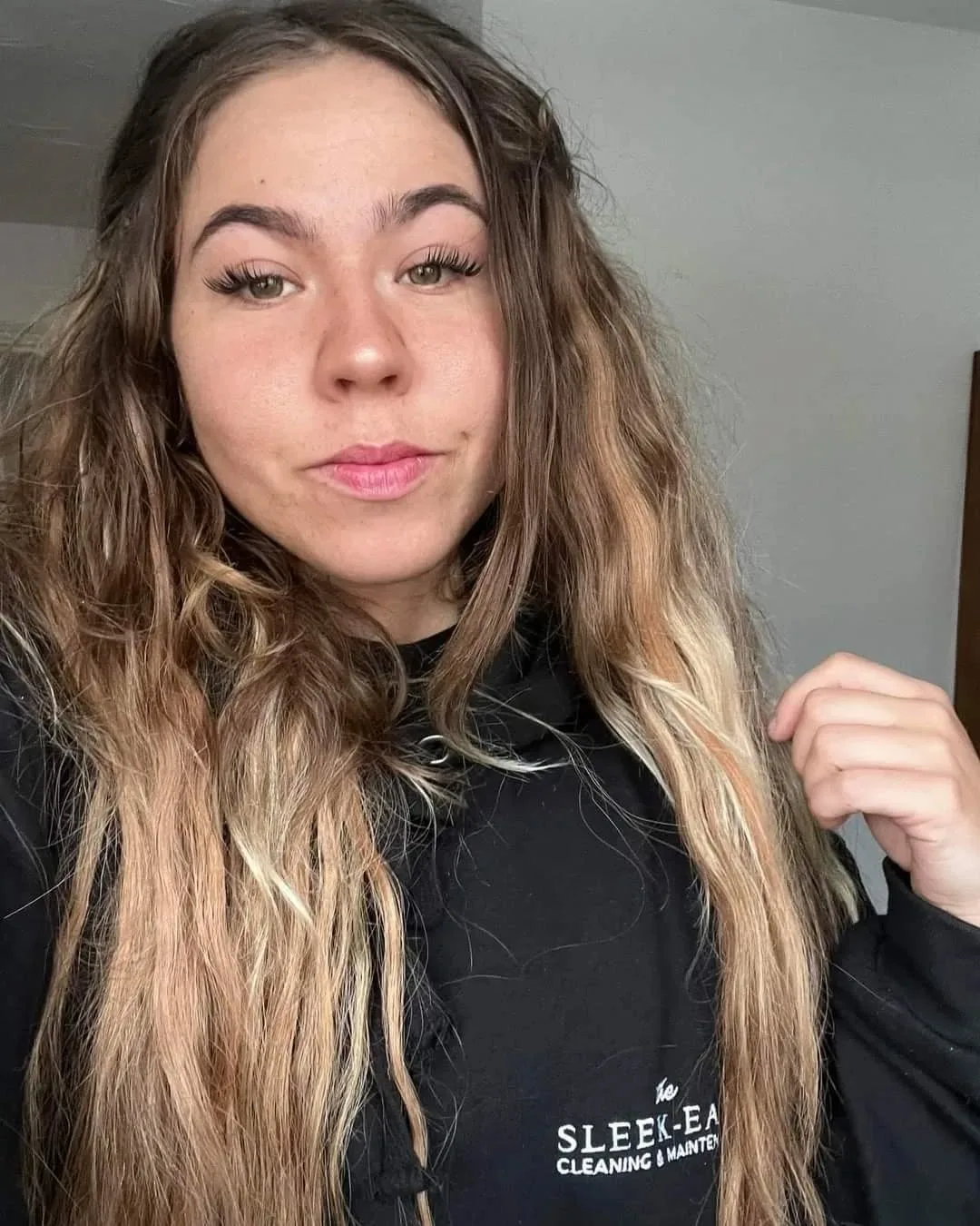 Girl with long blonde hair and long eyelashes wearing black jumper and looking into camera.