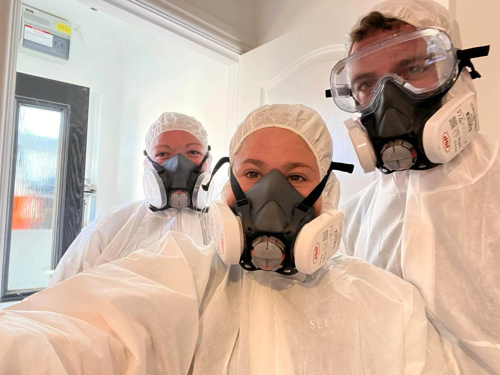 Two women and one man in white biohazard clothing.