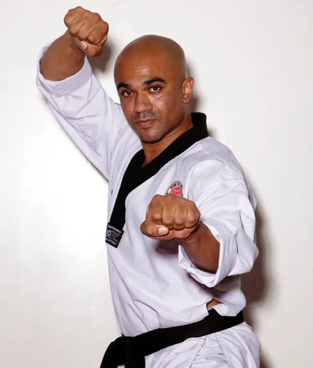 Man in taekwondo gear holding up a pose and staring into camera.