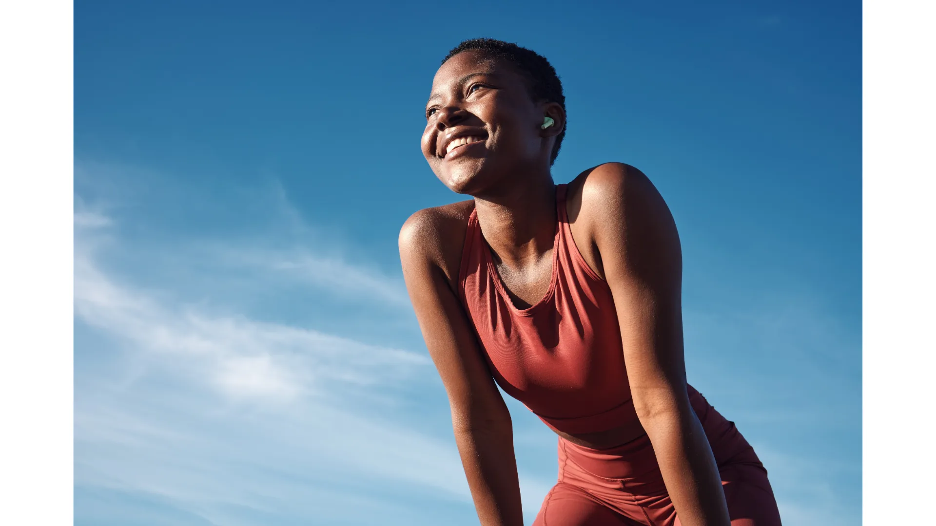 A woman smiles with the sky behind her during an outdoor workout.