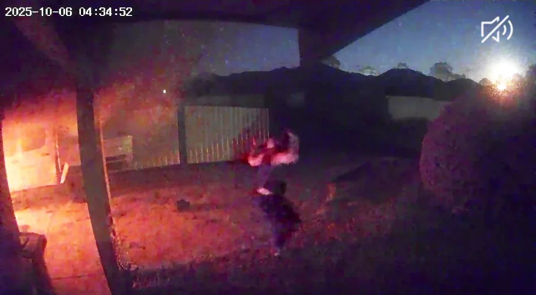 Dark footage of woman standing with arms up wile fire burning behind her.
