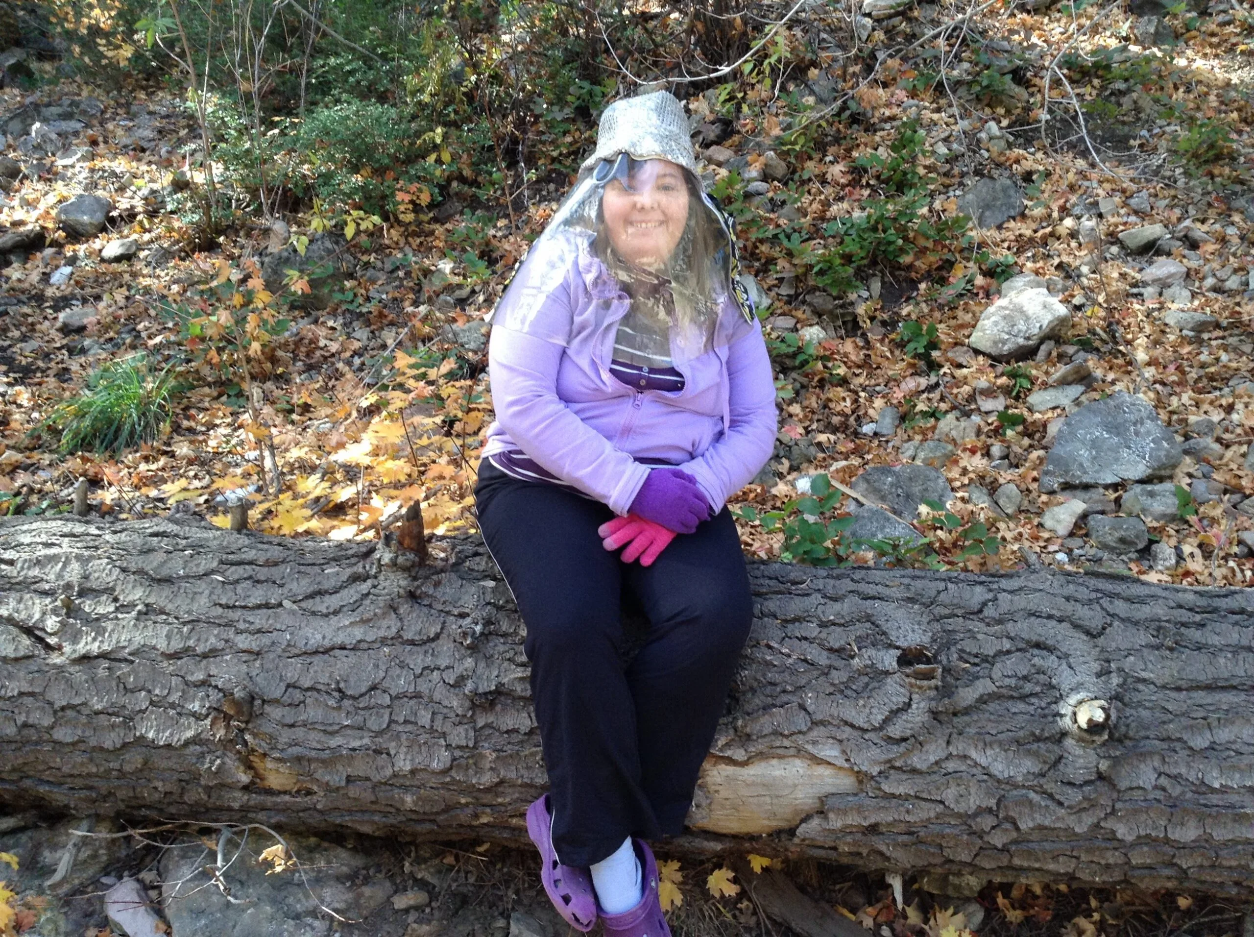 woman in PPE sitting on log outside 