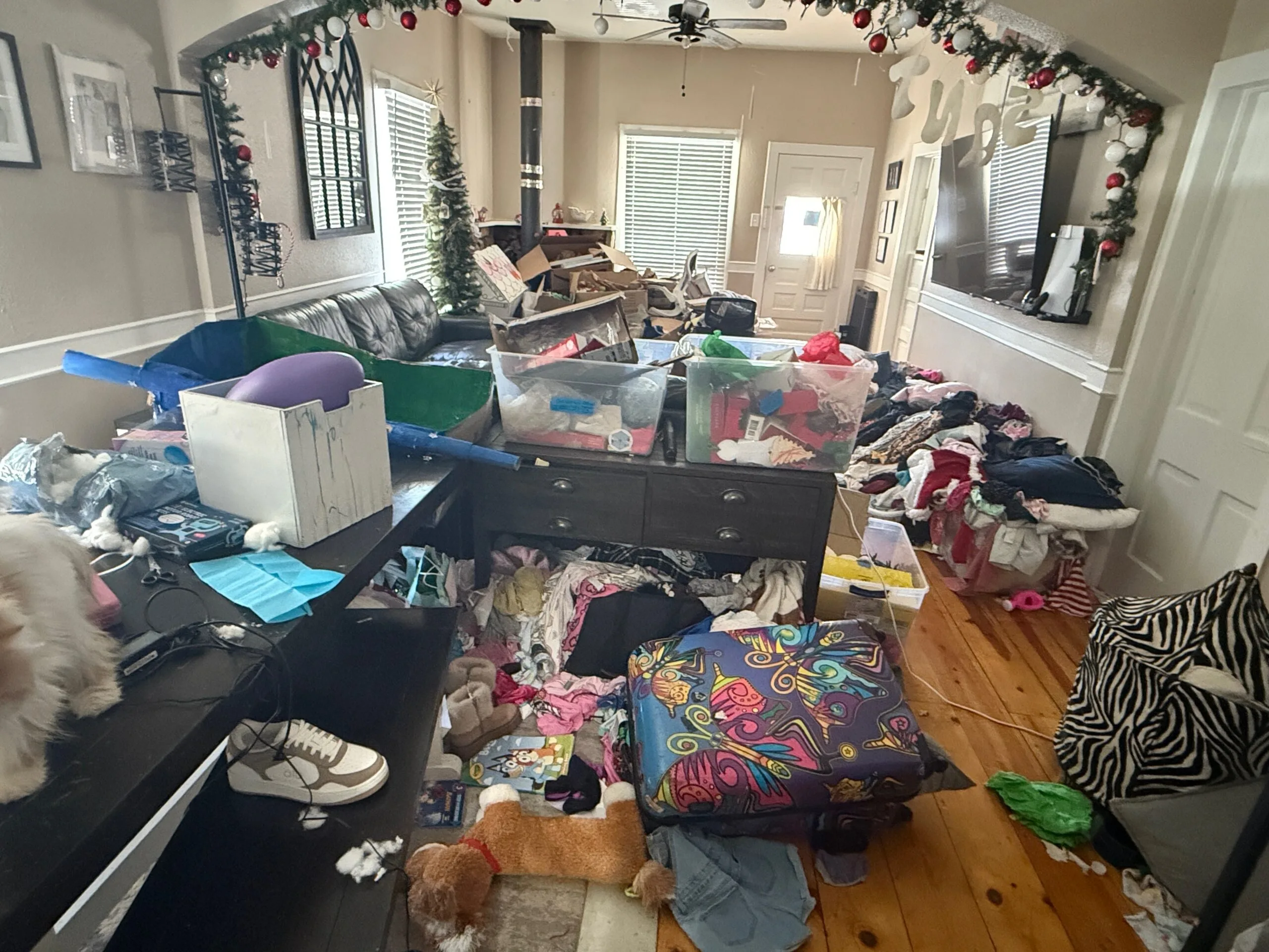 Image of living room with piles of clothes, boxes and rubbish stacked all across the floor.