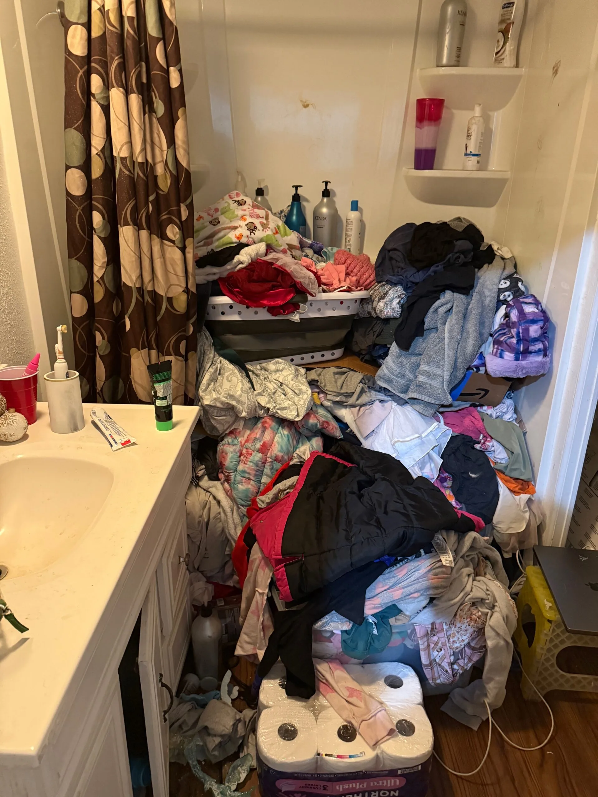 Image of bathtub with baskets of clothes, toilet rolls, shampoo bottles and soap piled up.