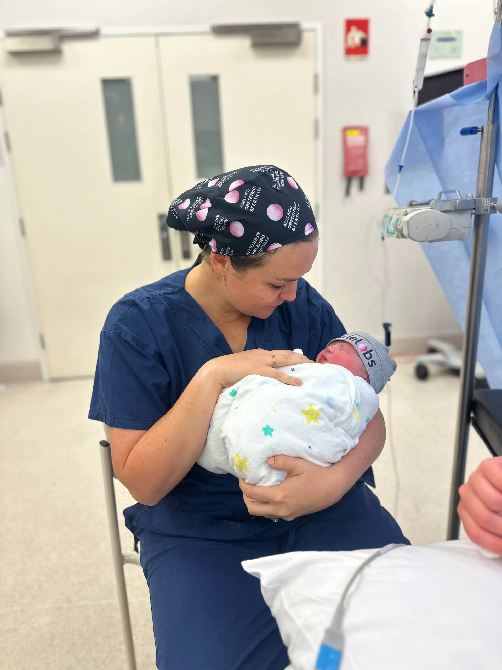 Woman in blue hospital scrubs and hair net holding newborn baby in arms.