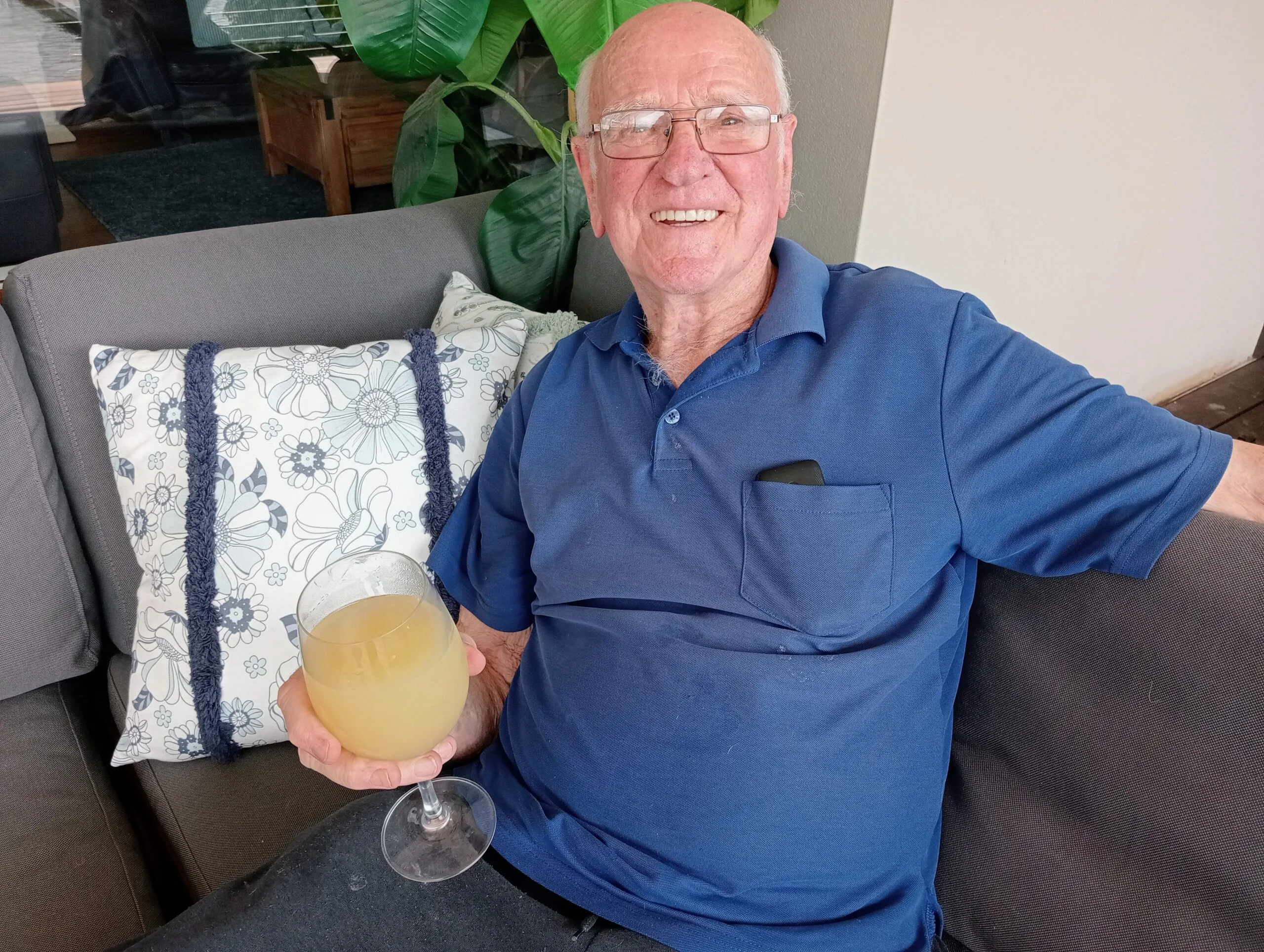 man in navy shirt sitting on couch drink in hand 