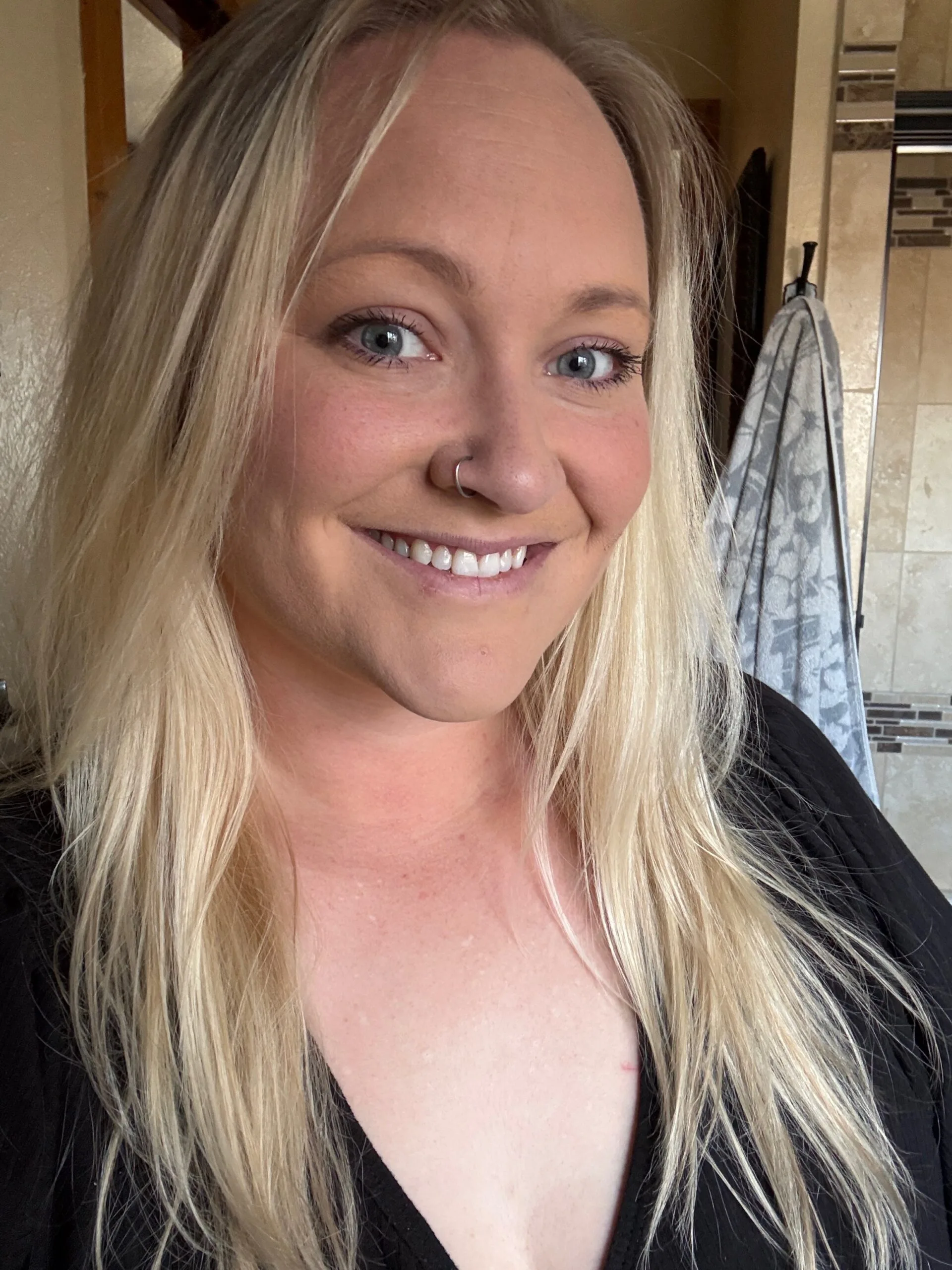 Woman with blonde hair and blue eyes wearing black shirt and smiling at camera.