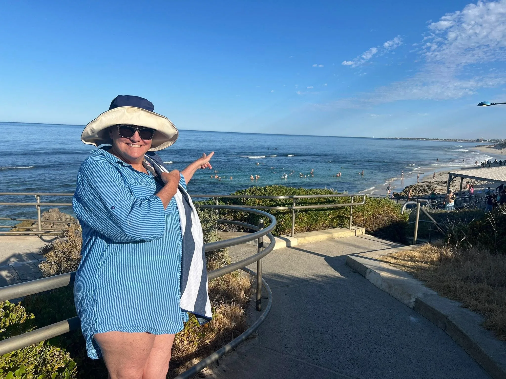 women in blue striped shirt and hat pointing to the beach