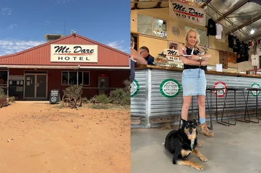 An outback pub in the desert with a woman holding a joey kangaroo with a kelpie at her feet