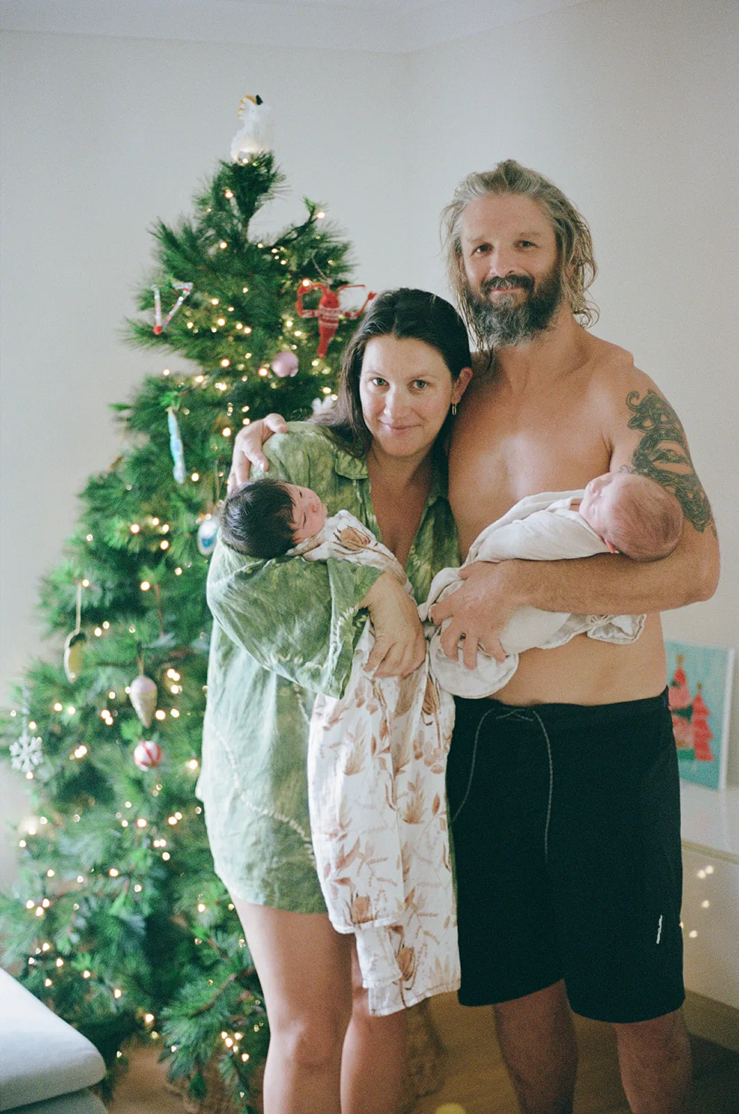 mum and dad both hold one twin each in front of the christmas tree