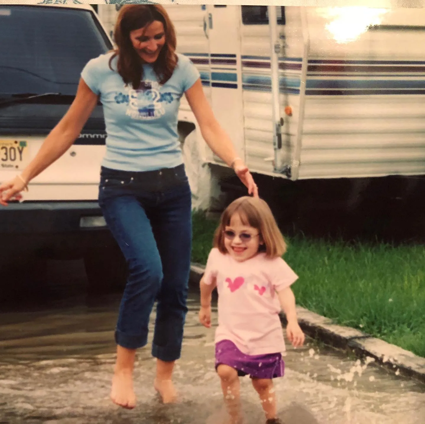 Photo of woman wearing blue shirt and jeans chasing after little girl wearing pink top and purple skirt.