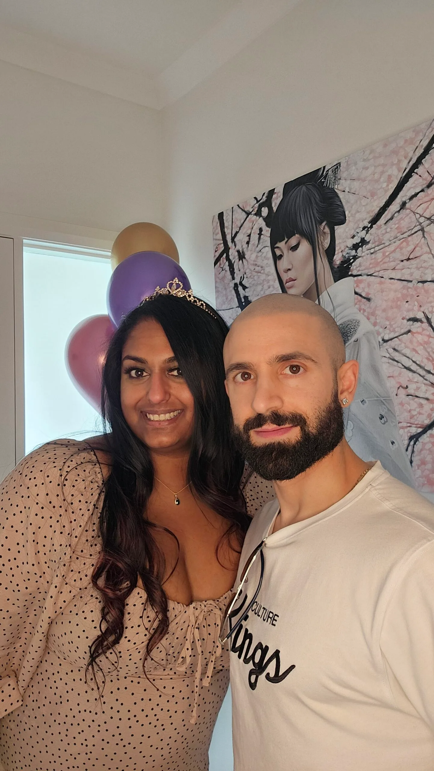 Left: Woman with black hair wearing brown dress and a tiara, smiling. 
Right: Man with black bear, wearing white shirt, wrapping arm around woman and smilling.
