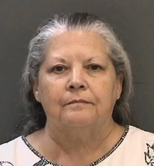 Woman with grey hair, wearing white top staring at camera.