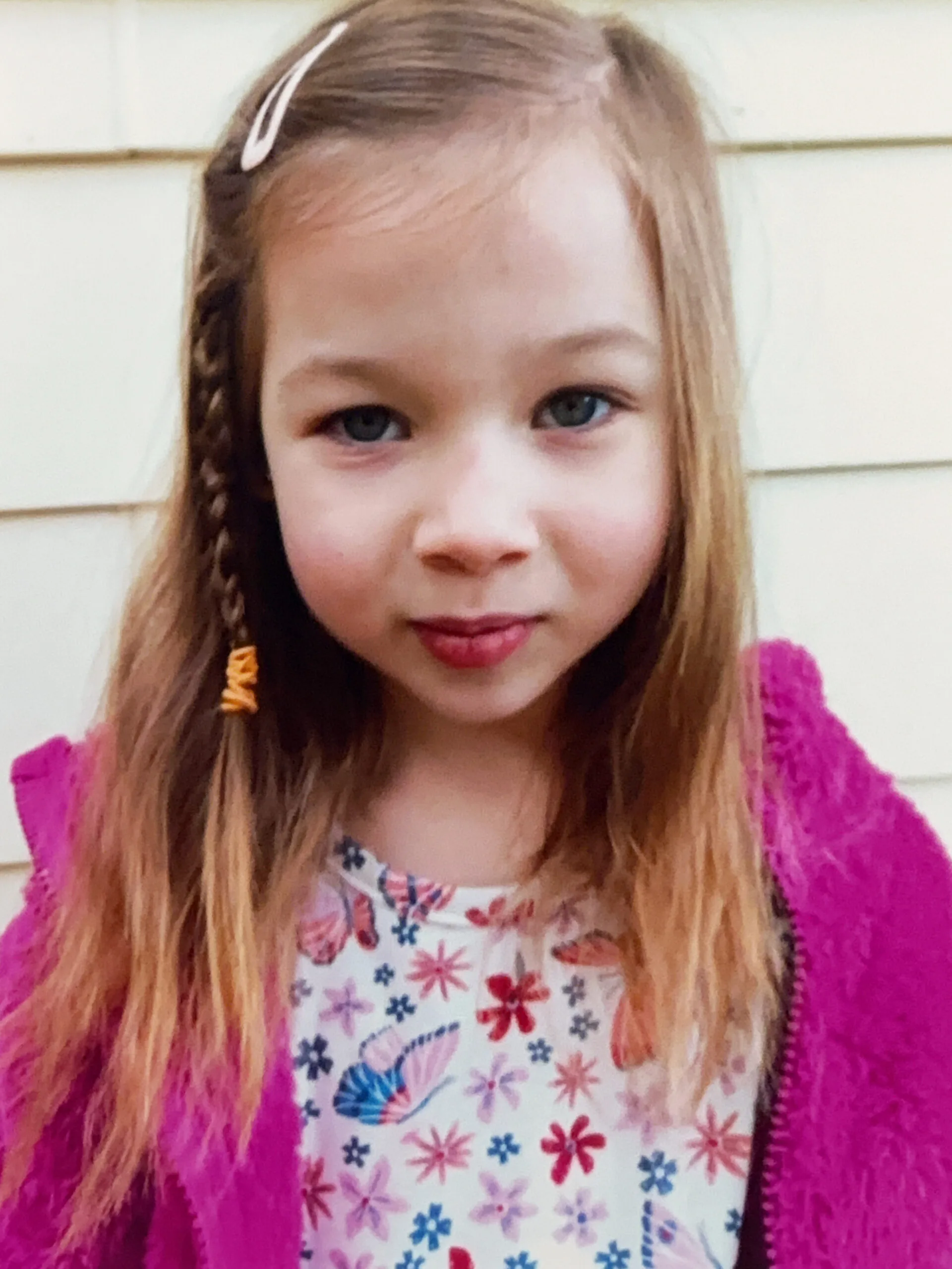 Little girl with long brown hair and blue eyes, wearing pink jacket and staring into camera.
