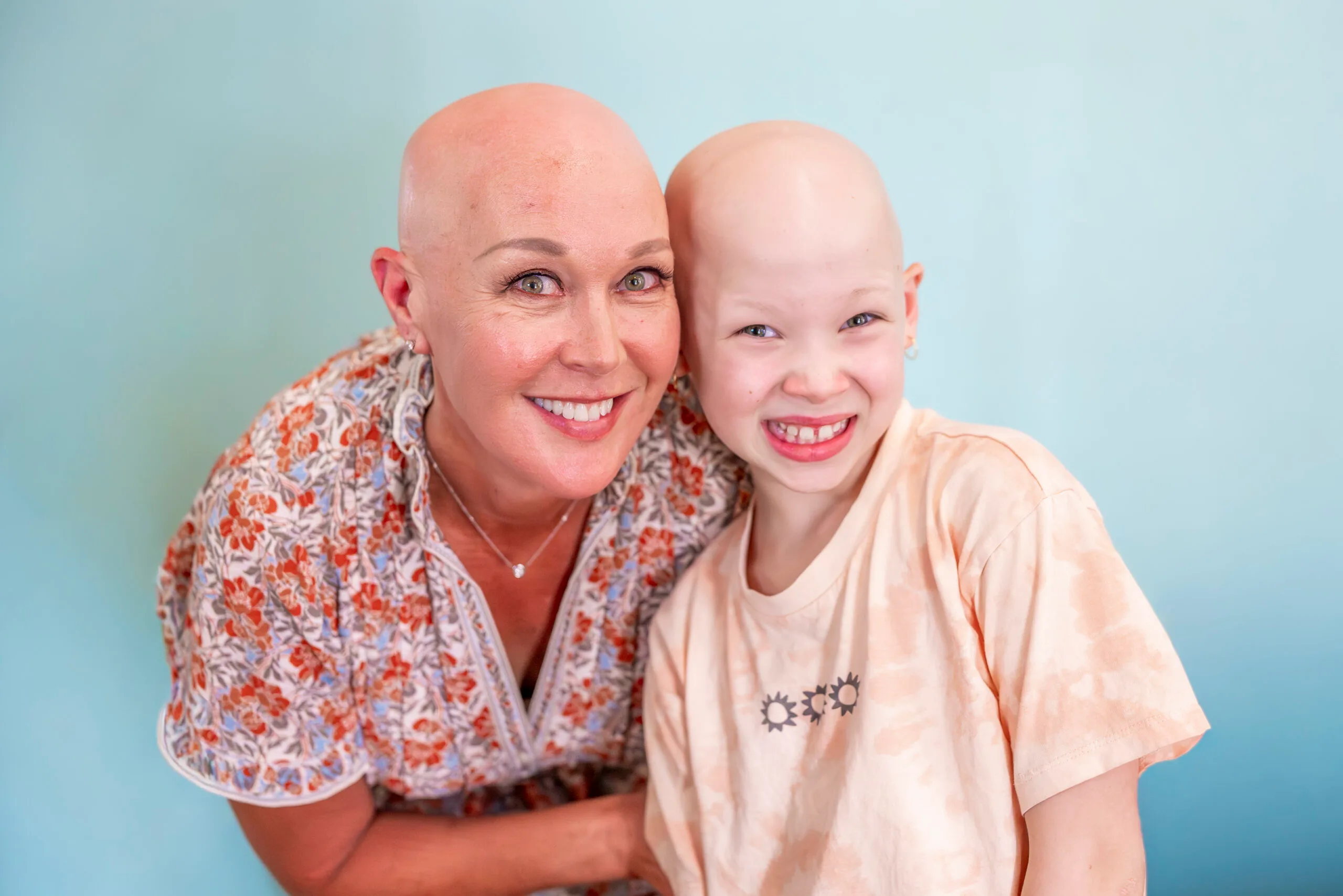 Woman and little girl, both with no hair, smilling at camera.