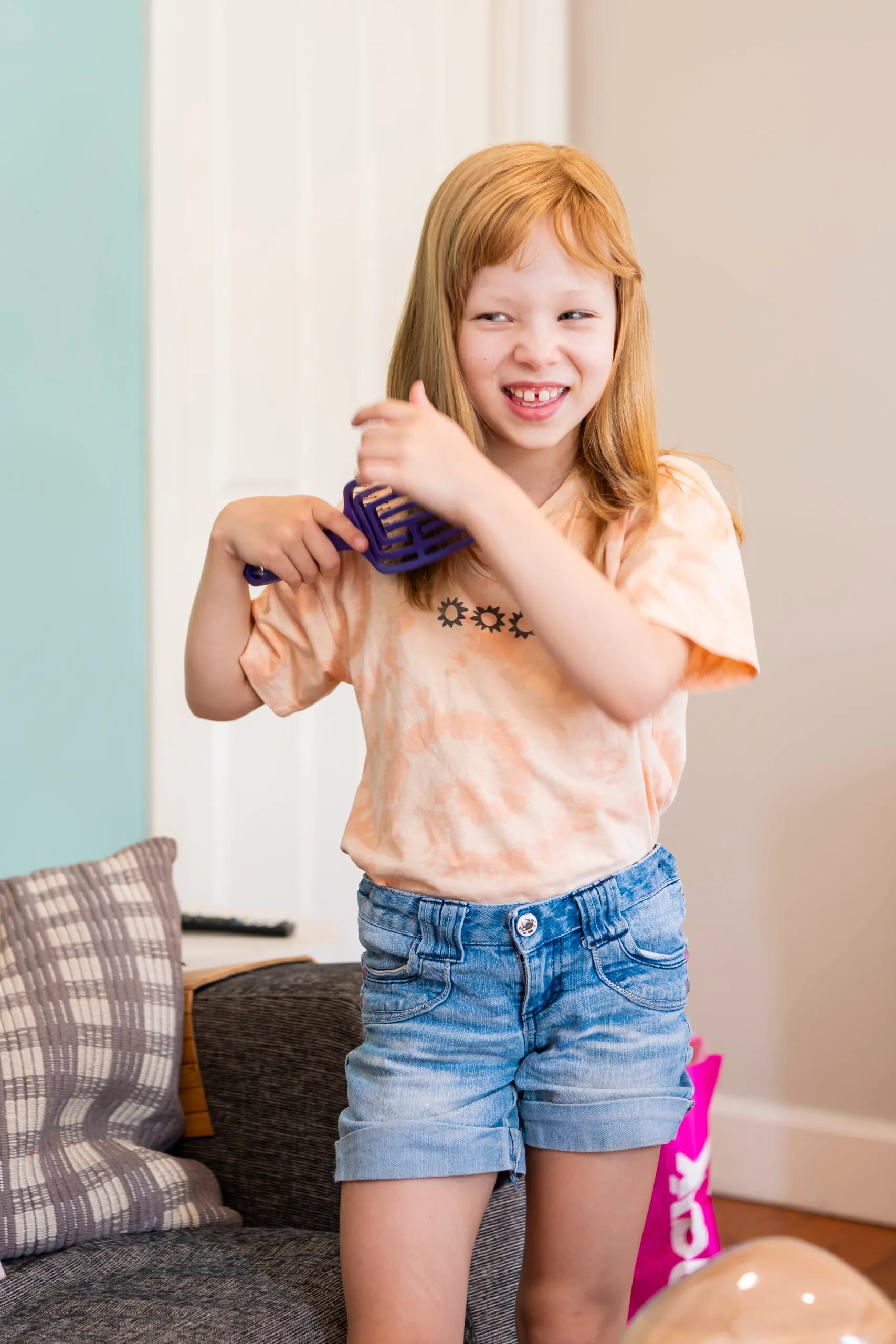 Young girl wearing blonde wig and brushing her hair while smilling away from camera.