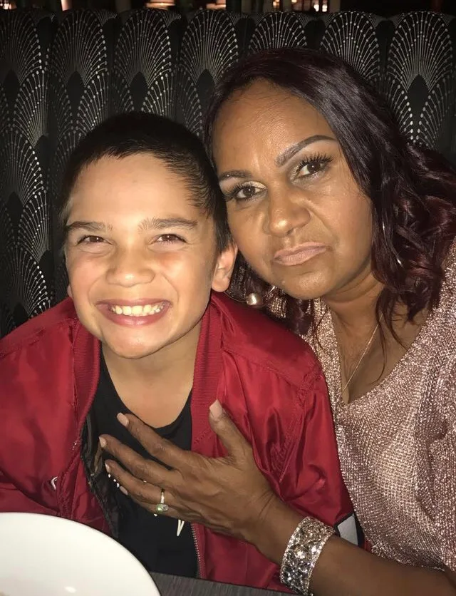 Woman and young boy sitting down at restaurant and smilling at camrea.